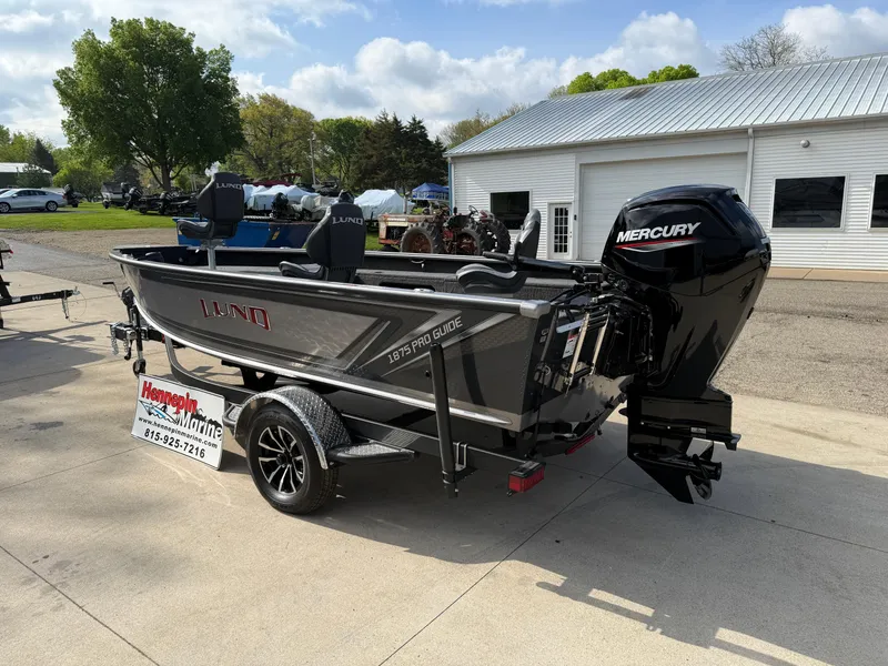 Slide: The Image of 2025 Lund 1875 Pro Guide boat with Mercury engine on trailer, parked outdoors. - 8