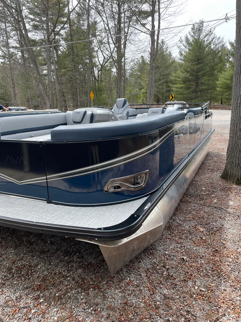 Slide: The Image of 2025 Avalon 25 LSZ Elite pontoon boat parked on gravel, surrounded by trees. - 5