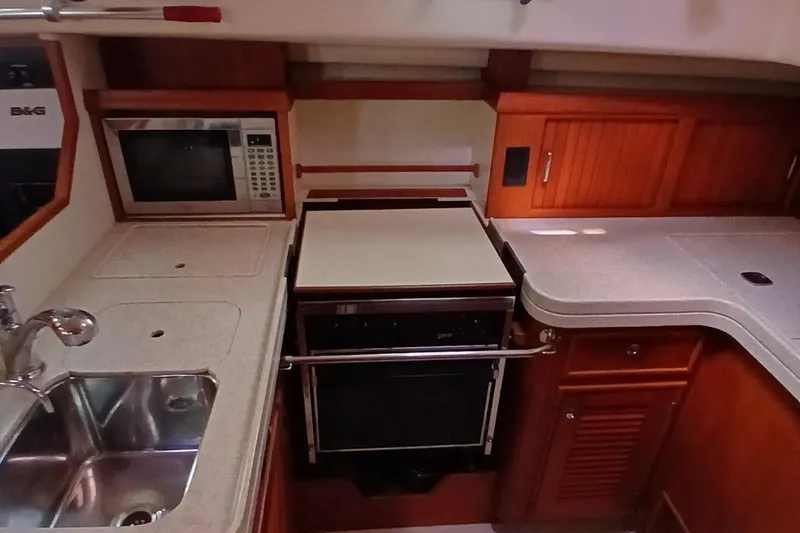 Slide: The Image of 2006 Island Packet 440 yacht kitchen with sink, stove, microwave, and wooden cabinetry. - 29
