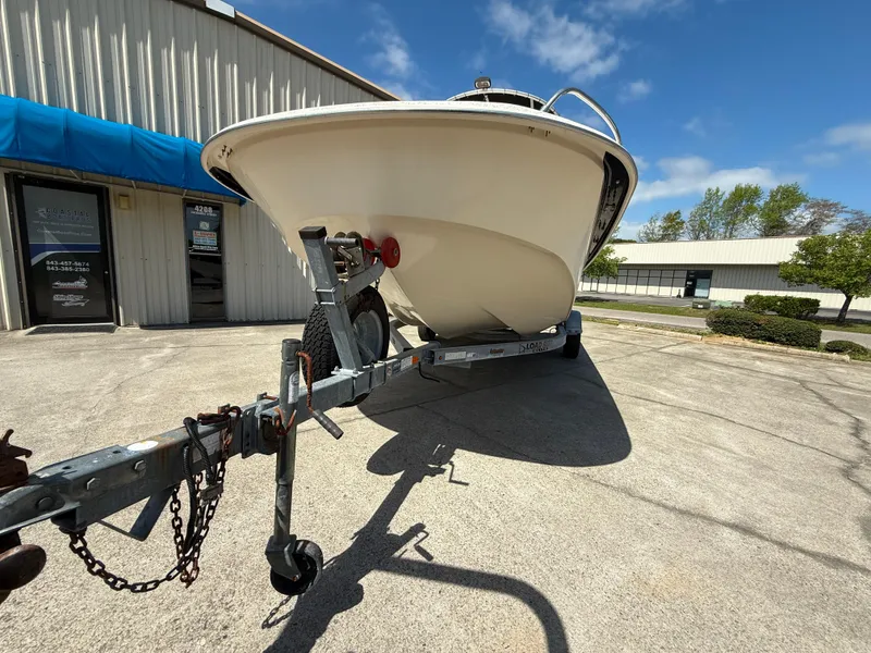 Slide: The Image of 2013 Carolina Skiff 218 DLV boat on trailer, parked outside a building under a clear sky. - 4