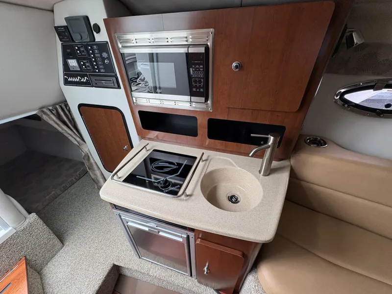 Slide: The Image of 2023 Crownline 264 CR boat interior with kitchenette, featuring microwave, stove, sink, and cabinetry. - 12