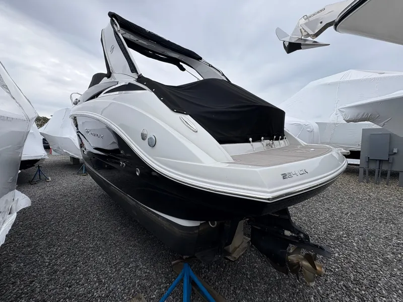 Slide: The Image of 2023 Crownline 264 CR boat with black cover, displayed outdoors on gravel. - 2