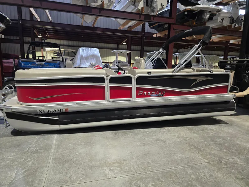 Slide: The Image of 2022 Premier 210 SunSation RE pontoon boat in storage, red and black design. - 0