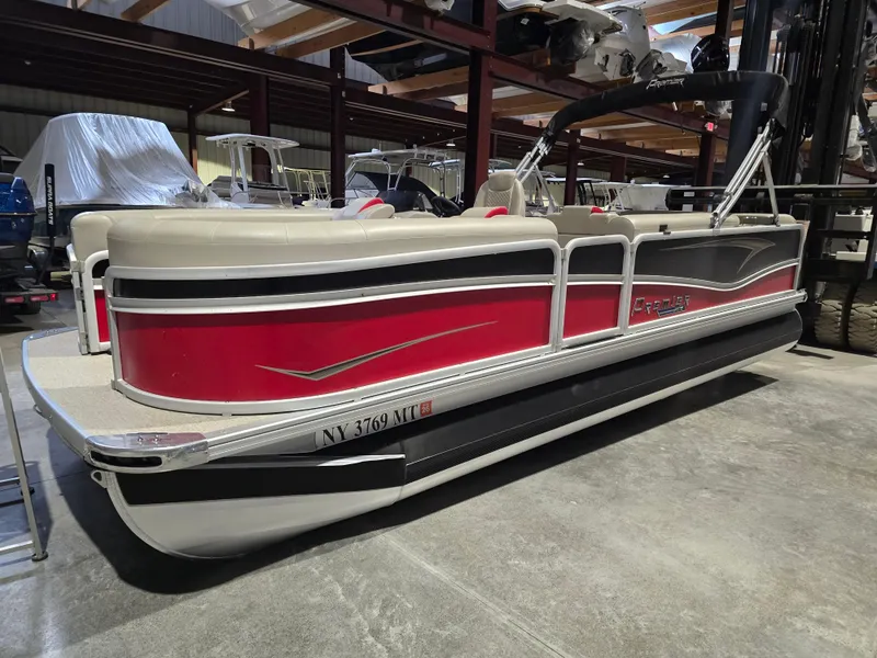 Slide: The Image of 2022 Premier 210 SunSation RE pontoon boat with red and beige design in storage facility. - 1
