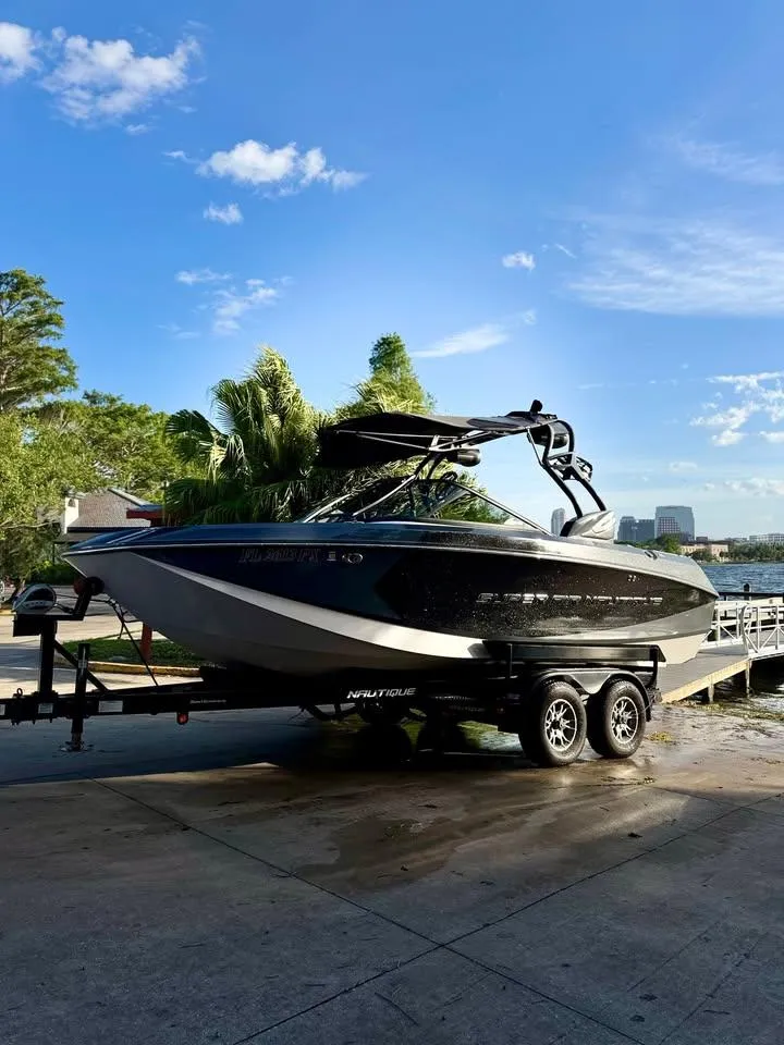 Slide: The Image of 2015 Nautique Super Air Nautique G21 boat on trailer, parked near water under blue sky. - 3