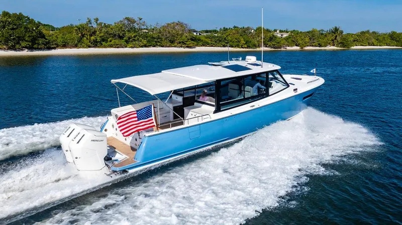 Slide: The Image of 2024 MJM 4 boat cruising on water, displaying an American flag, with lush greenery in the background. - 16
