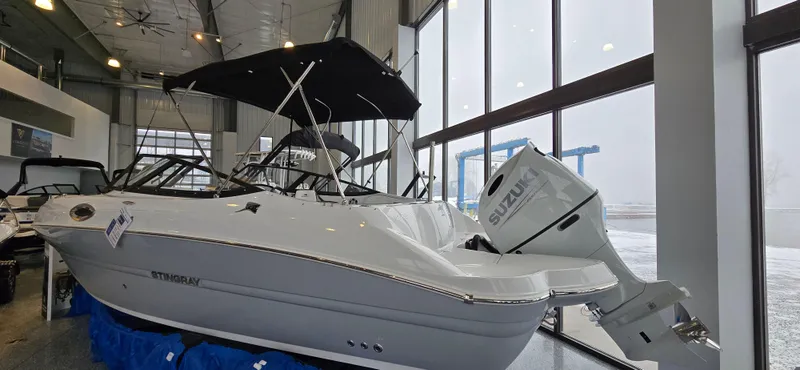 Slide: The Image of 2025 Stingray 211DC boat displayed indoors with Suzuki outboard motor. - 19