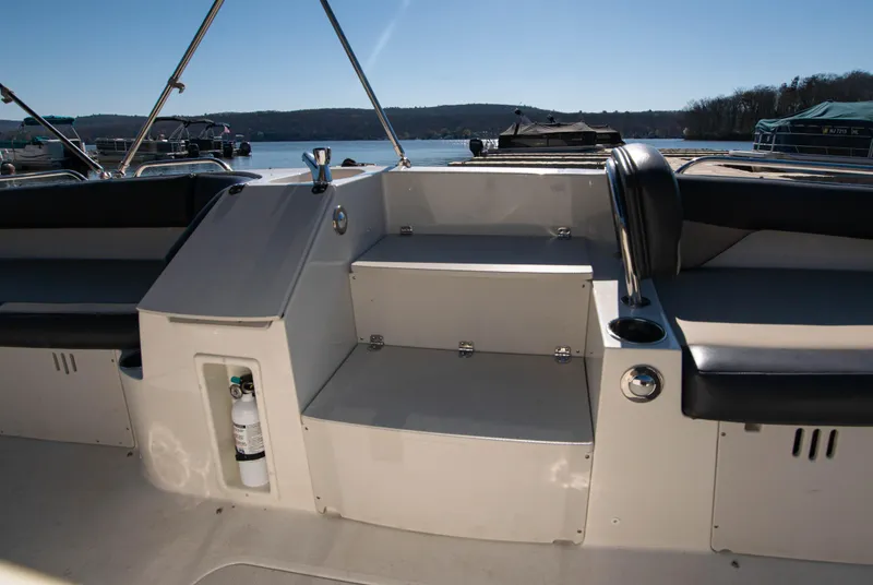Slide: The Image of 2019 Stingray 212 SC boat interior with seating and storage, docked by a scenic lake. - 11