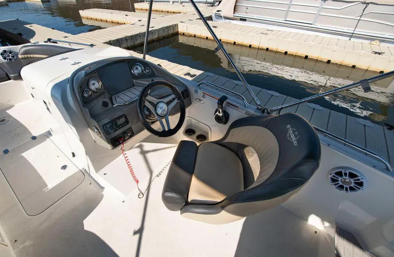 Slide: The Image of 2019 Stingray 212 SC boat interior with steering wheel and comfortable seating at dock. - 16