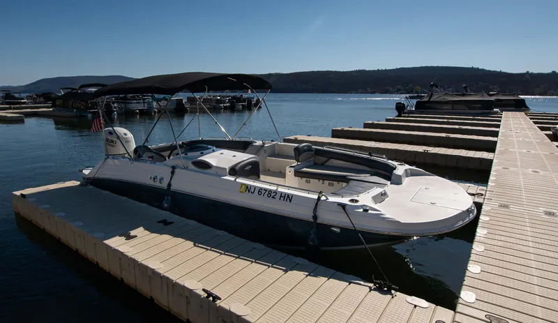 Slide: The Image of 2019 Stingray 212 SC boat docked on a sunny lake with scenic background. - 2