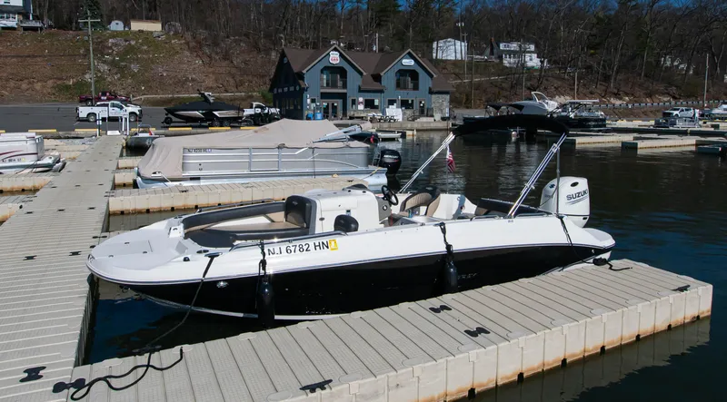 Slide: The Image of 2019 Stingray 212 SC boat docked at a marina with surrounding boats and buildings. - 6