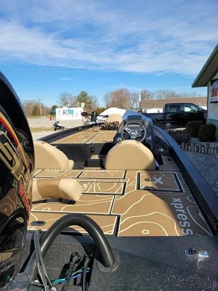 Slide: The Image of 2023 Xpress X21 Pro boat with tan interior, parked outdoors under a clear blue sky. - 2