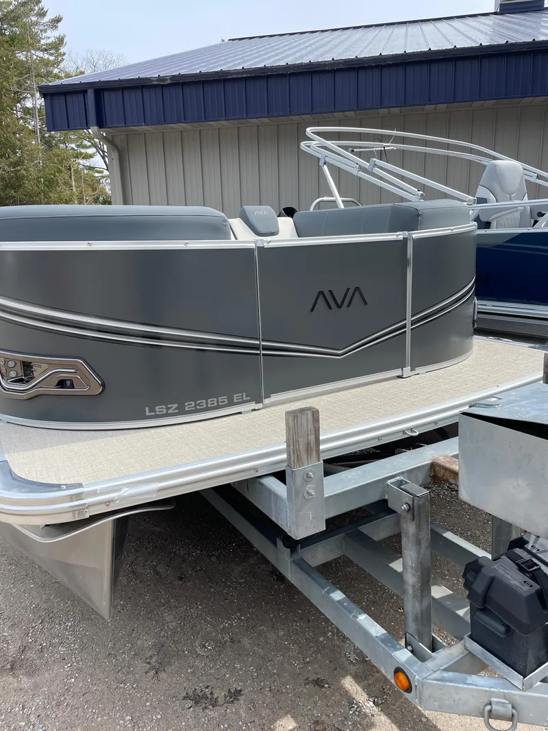 Slide: The Image of 2025 Avalon 23 LSZ Elite pontoon boat on trailer, gray exterior, docked near building. - 3
