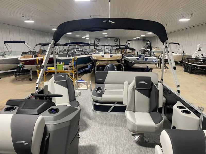 Slide: The Image of 2025 Bennington 22SSB-SPS pontoon boat in showroom, featuring modern seating and canopy. - 16