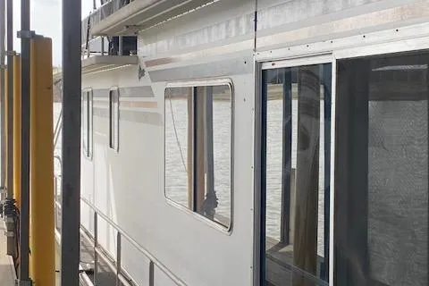Slide: The Image of 1985 Sumerset 60 X 14 houseboat docked, showcasing side view and windows. - 12