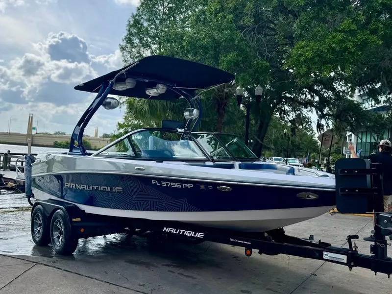 Slide: The Image of 2011 Nautique 200V boat on trailer, parked outdoors with trees in the background. - 0