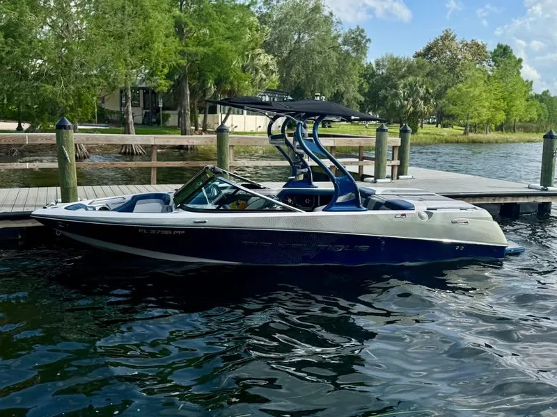 Slide: The Image of 2011 Nautique 200V boat docked on a serene lake with lush greenery. - 1