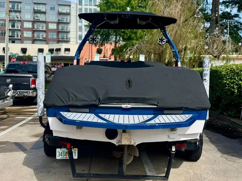 Slide: The Image of 2011 Nautique 200V boat, covered, parked in urban setting with buildings in background. - 2