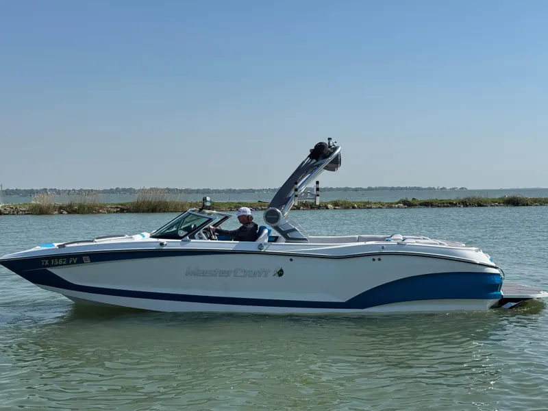 Slide: The Image of 2019 MasterCraft X24 boat cruising on a calm lake under a clear blue sky. - 1