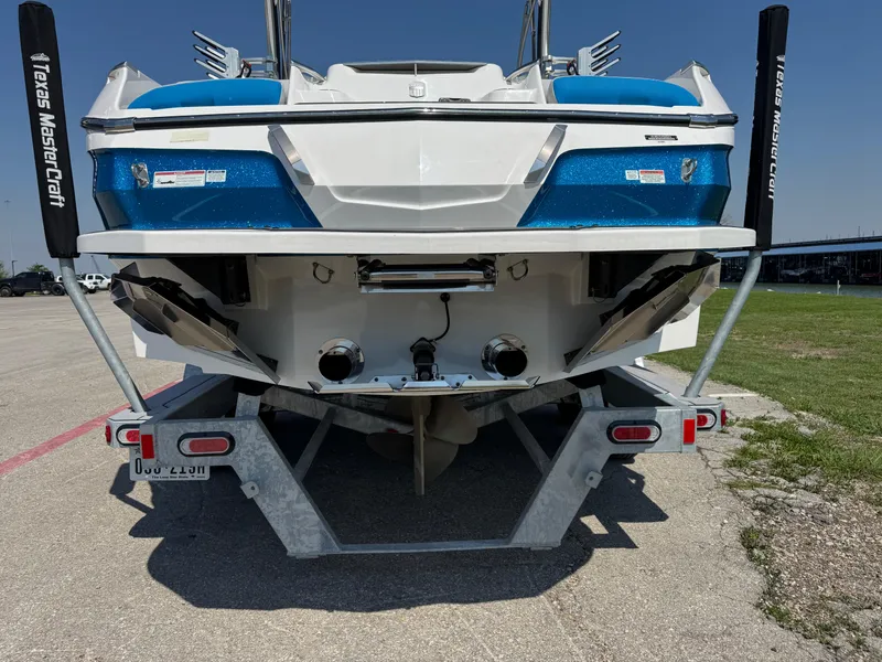 Slide: The Image of 2019 MasterCraft X24 boat rear view on trailer, showcasing dual exhaust and blue accents. - 11