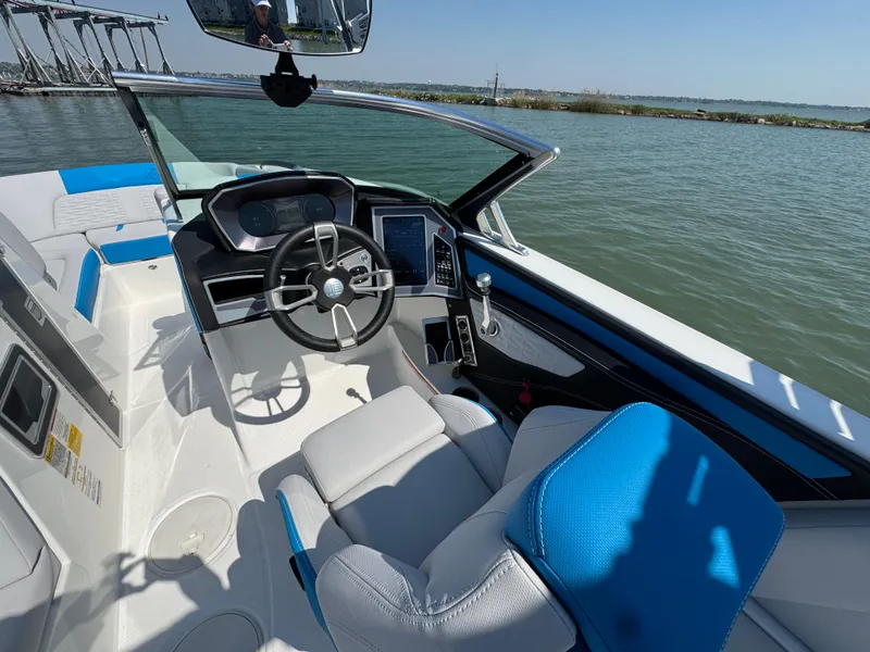 Slide: The Image of 2019 MasterCraft X24 boat interior with steering wheel, blue and white seating, on a sunny day. - 17