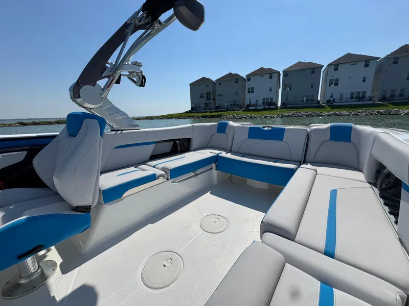 Slide: The Image of 2019 MasterCraft X24 boat interior with white and blue seating, near waterfront homes. - 19