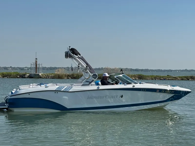 Slide: The Image of 2019 MasterCraft X24 boat cruising on a calm lake under a clear blue sky. - 2