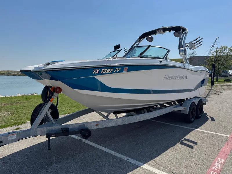 Slide: The Image of 2019 MasterCraft X24 boat on trailer, parked near a lake under clear skies. - 8