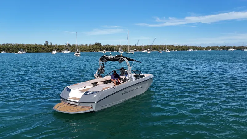 Slide: The Image of 2018 Nautique Super Air Nautique G25 boat on calm blue water with trees in background. - 13
