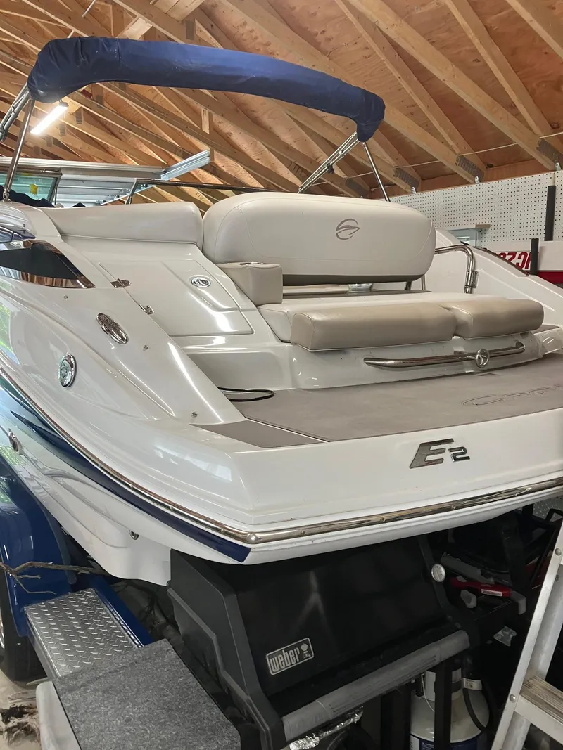Slide: The Image of 2012 Crownline E2 Eclipse boat in a wooden garage, featuring a blue canopy and cushioned seating. - 6