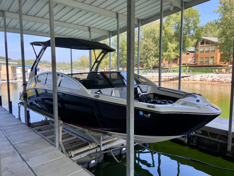 Slide: The Image of 2019 Yamaha Boats 275 SE docked under a covered marina, surrounded by trees and buildings. - 11