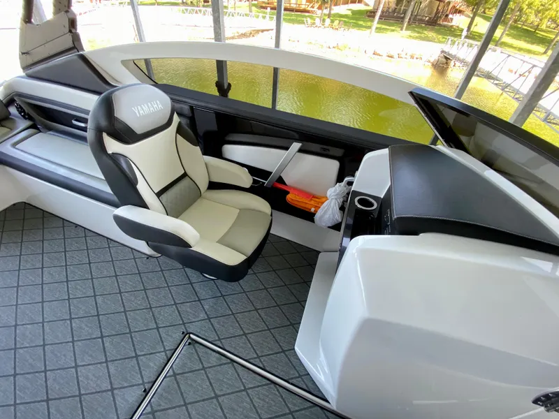 Slide: The Image of 2019 Yamaha Boats 275 SE interior with captain's chair and dashboard, docked by a lake. - 25