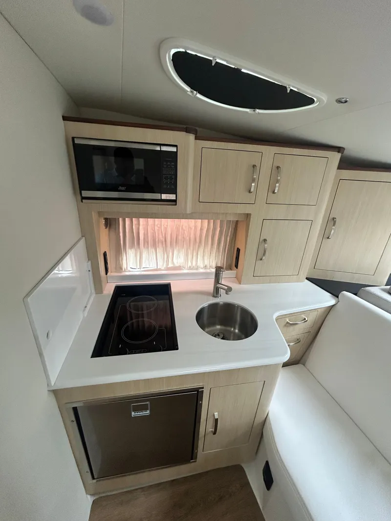 Slide: The Image of 2024 Regal 33 XO yacht kitchen with stove, sink, microwave, and cabinetry. - 10