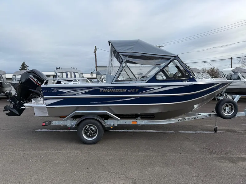 Slide: The Image of 2025 Thunder Jet 185 Luxor boat on trailer, blue and silver design, parked outdoors. - 1