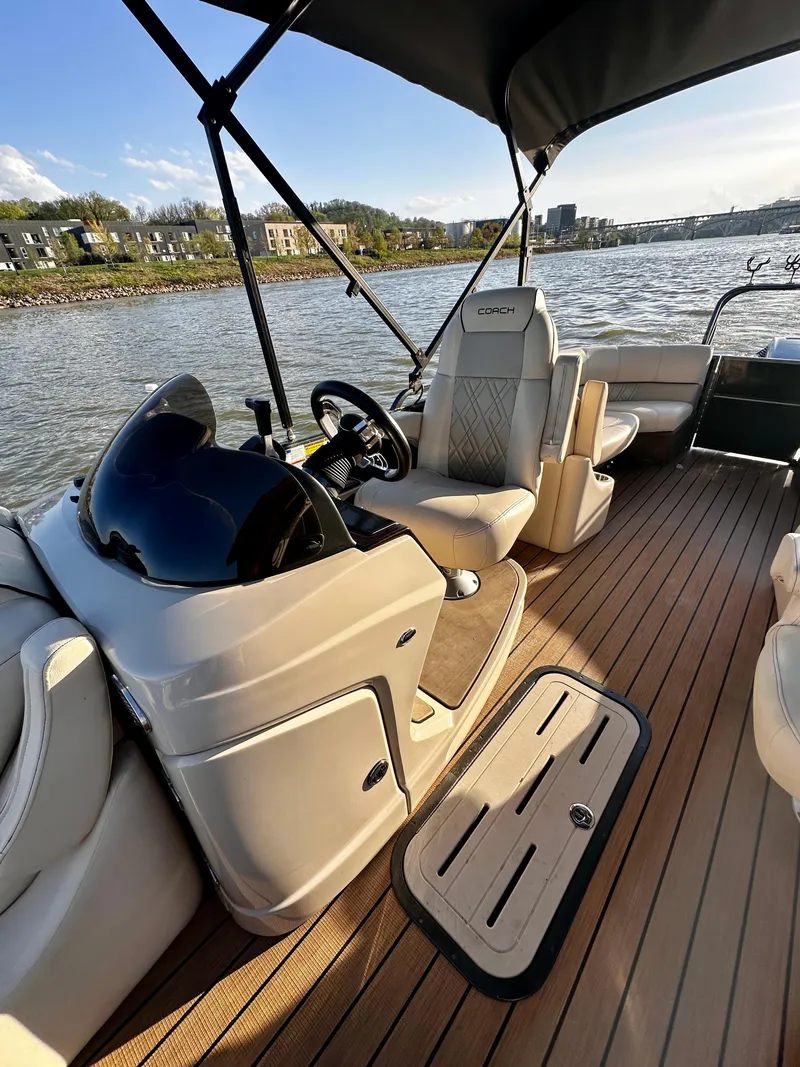 Slide: The Image of 2019 Coach Pontoons 230 RF interior with steering console, seating, and wood-style flooring on a lake. - 10