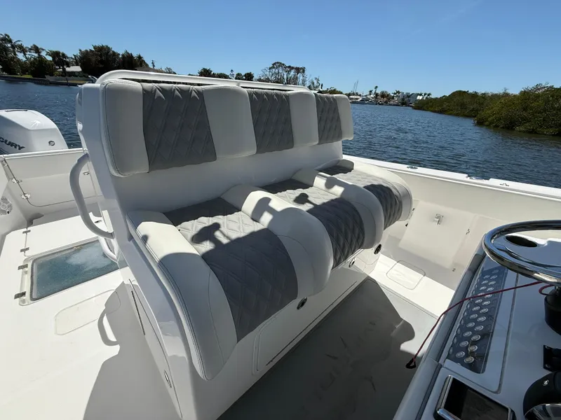 Slide: The Image of 2022 Invincible 33 Catamaran with cushioned seating, steering console, and scenic water backdrop. - 14