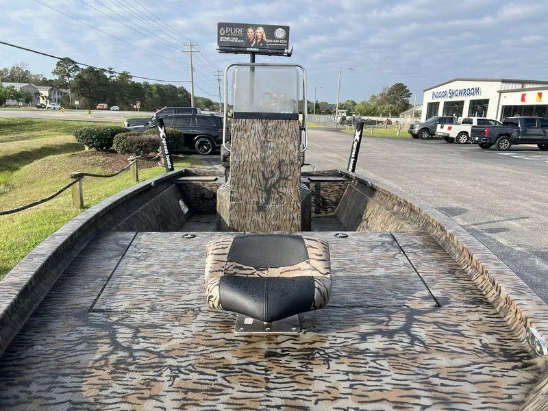 Slide: The Image of 2025 Xpress H210 BAY boat with camouflage design, parked outdoors near a showroom. - 14