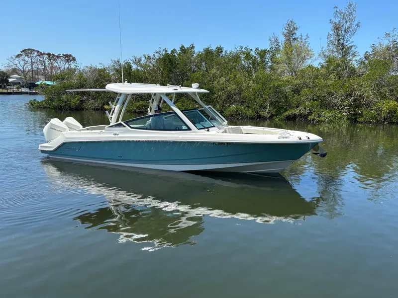 Slide: The Image of 2023 Boston Whaler 280 Vantage boat on calm water, surrounded by lush greenery. - 1