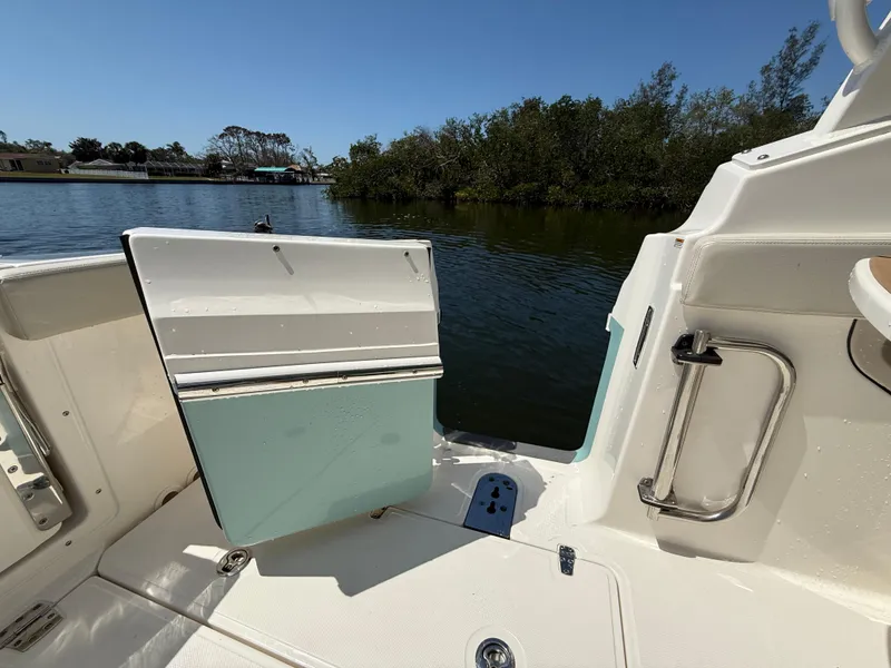 Slide: The Image of 2023 Boston Whaler 280 Vantage boat with open side door, near water and greenery. - 12