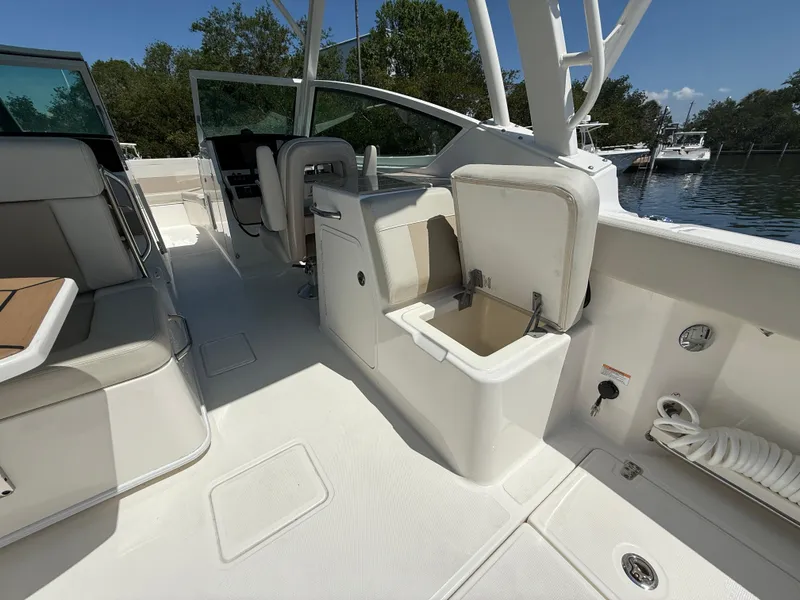 Slide: The Image of 2023 Boston Whaler 280 Vantage interior with seating and storage, docked by a serene waterfront. - 13