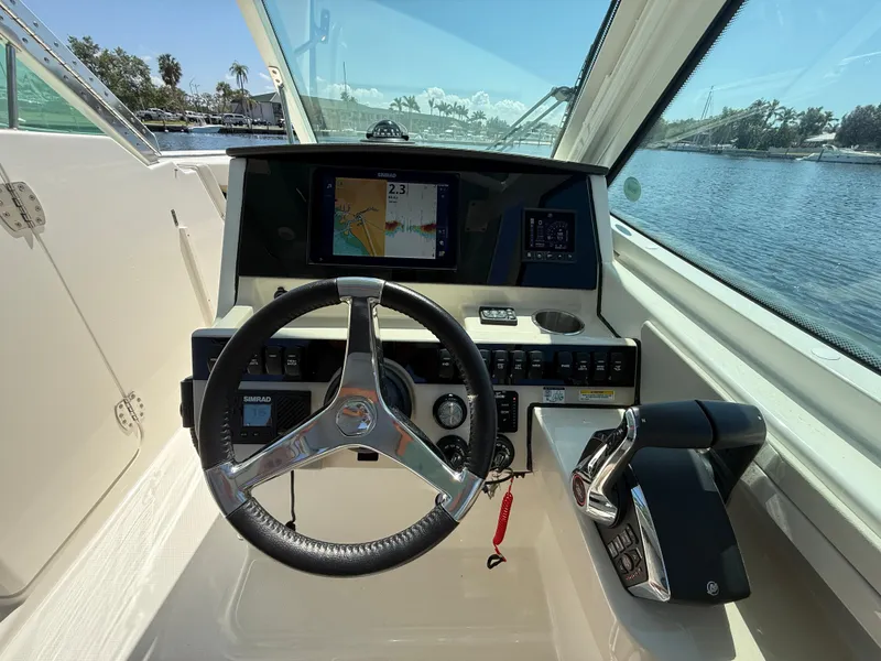 Slide: The Image of 2023 Boston Whaler 280 Vantage helm with steering wheel and navigation screens, docked by the water. - 21