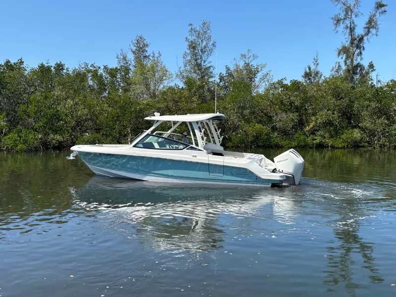 Slide: The Image of 2023 Boston Whaler 280 Vantage boat cruising on calm water near lush greenery. - 6