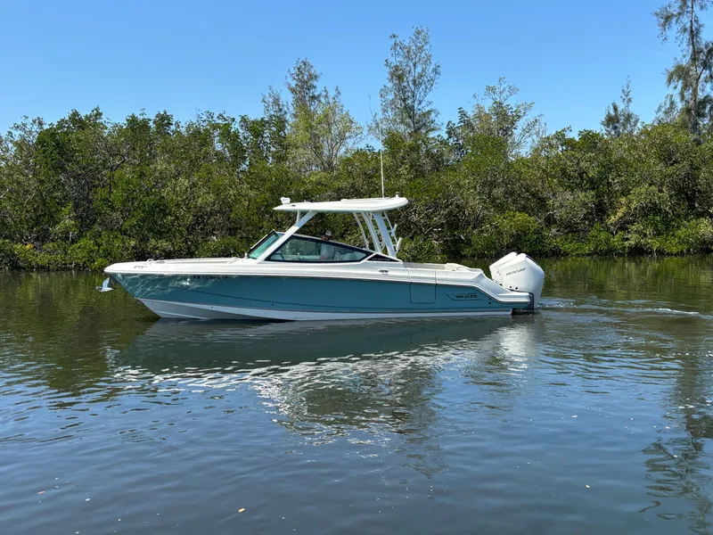 Slide: The Image of 2023 Boston Whaler 280 Vantage boat cruising on a calm river, surrounded by lush greenery. - 7