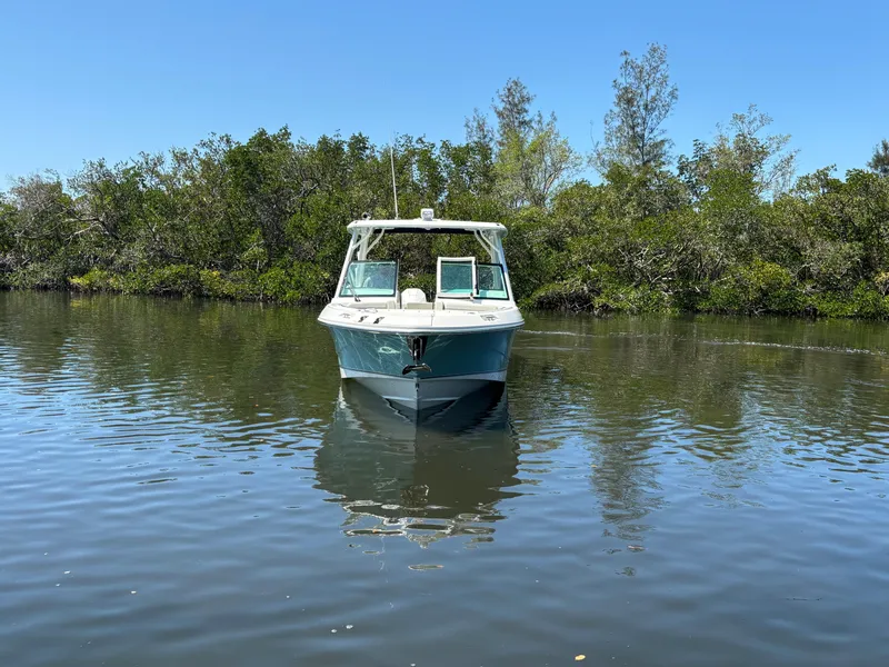 Slide: The Image of 2023 Boston Whaler 280 Vantage boat on calm water, surrounded by lush greenery. - 8