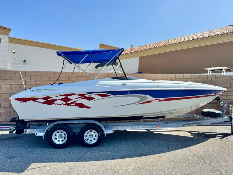 The Image of 2002 Baja 24H2X speedboat with red and blue graphics on a trailer, parked outdoors. - 0