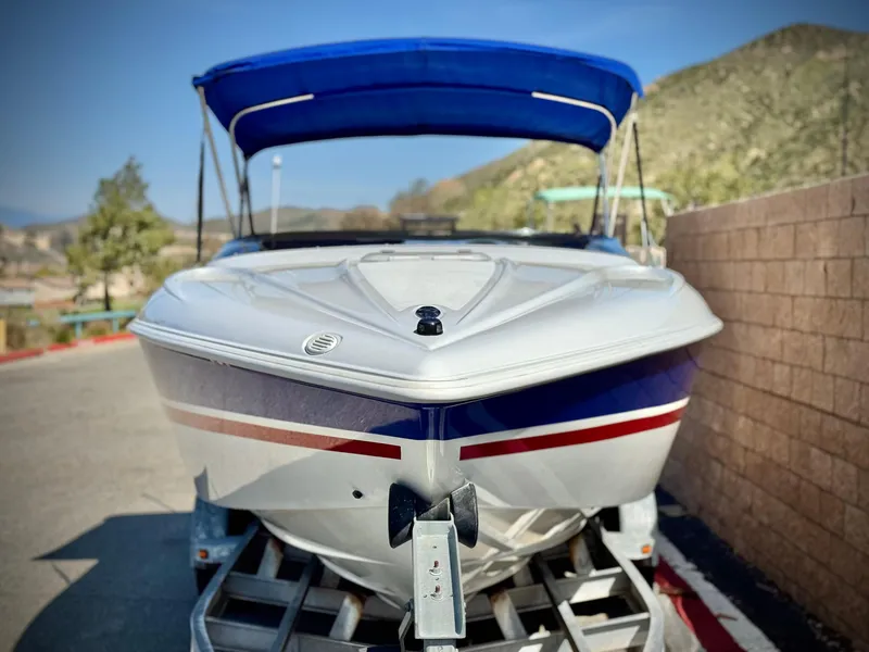Slide: The Image of 2002 Baja 24H2X boat with blue canopy on trailer, parked outdoors. - 2