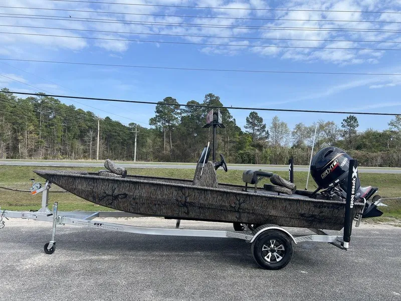 Slide: The Image of 2025 Xpress XP18CC boat on trailer, camo design, parked outdoors under blue sky. - 1