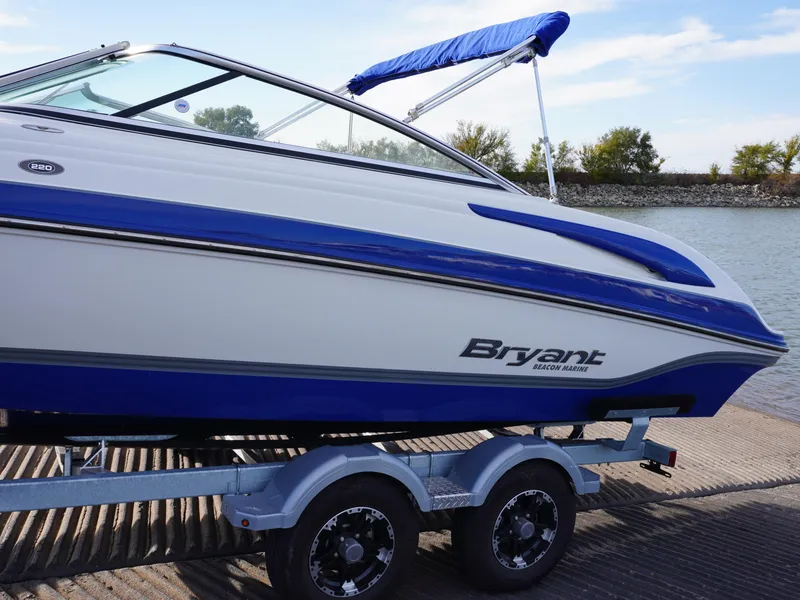 Slide: The Image of 2013 Bryant 220 boat on trailer by the water, featuring blue and white design. - 5