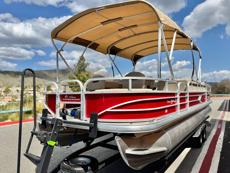 Slide: The Image of 2019 Sun Tracker Fishin' Barge 24 DLX pontoon boat on trailer, under blue sky. - 4
