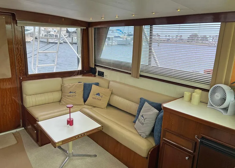 Slide: The Image of 1976 Hatteras Convertible yacht interior with beige seating, table, and large windows overlooking the water. - 20